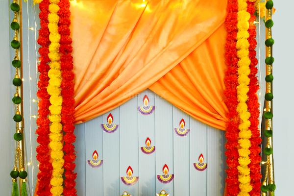 Transform Your Home into a Festive Haven with a Cuboid Stand, Orange and Yellow Garlands, Green Silk Hangings, Diya Paper Cutouts, and more.