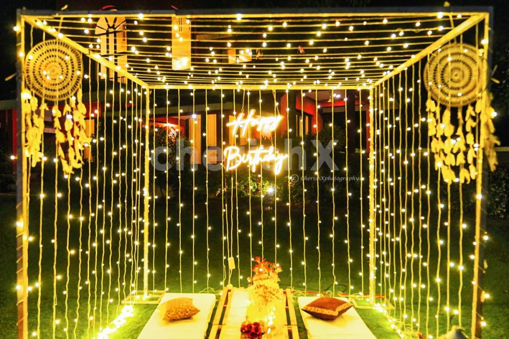 Wooden crates decorated with floor lamps, jute mats, and vases filled with artificial flowers, create a whimsical atmosphere in the cabana.