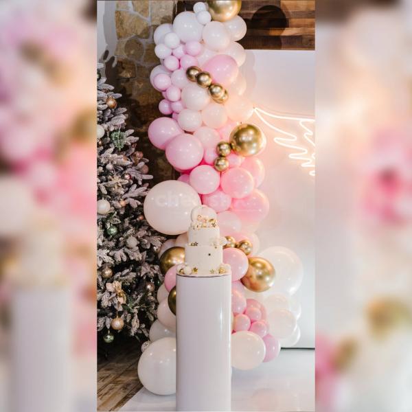 Experience the magic of the heartwarming baby shower decor with a backdrop of pink flex, adorned with a winged neon light and an arch of balloons in white, pastel pink, blush pink, and chrome, creating a whimsical and charming ambiance.