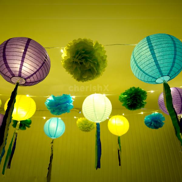 A variety of lanterns in purple, light blue, light green, and dark blue, illuminate the festive setting.